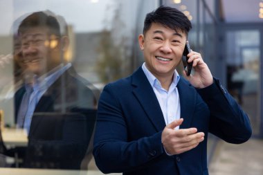 İletişim. Elinde telefon olan takım elbiseli genç Asyalı adam.