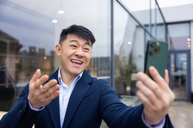 İletişim. Elinde telefon olan takım elbiseli genç Asyalı adam.