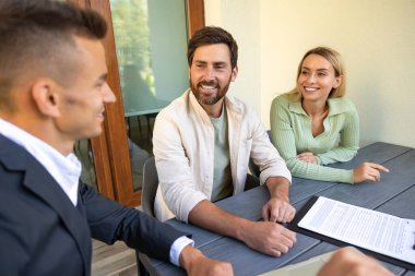 Emlakçı, güneşli bir günde laptopta çiftlerle anlaşma yapıyor.