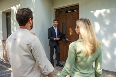 Emlakçı, güneşli havada modern ev turunda çifte kapı açıyor.