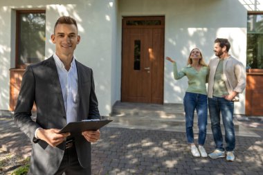 Takım elbiseli bir adam açık gökyüzü olan yeşil banliyö ortamında ev ev geziyor.
