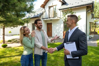 Güneşli bir günde modern evin önünde emlakçıyla tokalaşan çift.