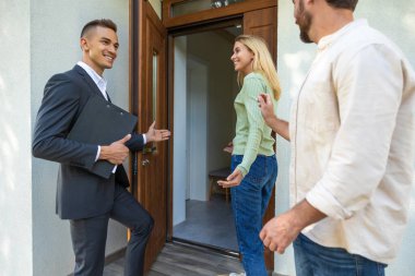 Emlakçı, çiftleri güneşli havada modern eve davet ediyor.