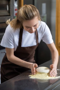 Kadın fırıncı tezgahta hamur yoğururken, önlük giyerken ve fırında çalışırken konsantre oluyor.