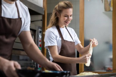 Sarışın bir kadın mutfak yüzeyinde iki eliyle hamur esnetiyor.