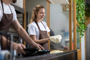 İki fırıncı, doğal ışıkla aydınlık bir mutfak ortamında çalışırken hamur hazırlamaya odaklanmış.