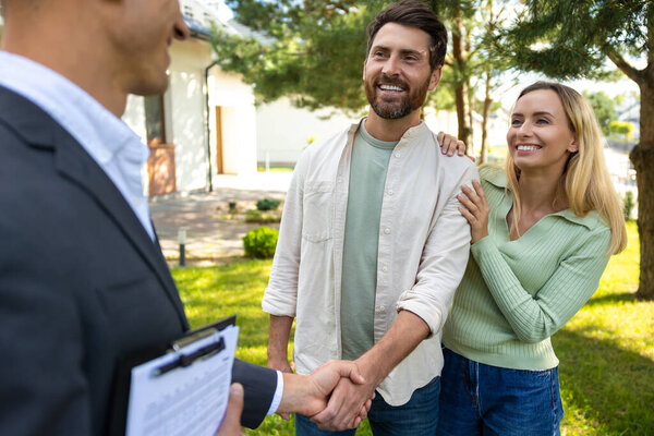 Пара рукопожатий с агентом по недвижимости за пределами современного дома в солнечный день