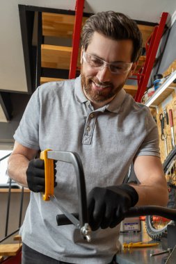 Bisiklet tamircisi, iyi aydınlatılmış atölyede ekipmanlarla çevrili bisikleti tamir etmek için aletler kullanıyor.