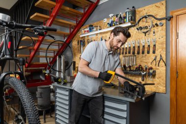 Profesyonel kıyafetli sakallı bir velomekanik. Atölye ayarlarında özel aletleri olan bisiklet tamircisi.