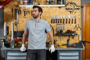 Gülümseyen sakallı adam beyaz eldivenlerle garajda dikiliyor.