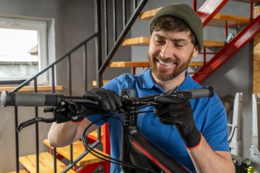 Sakallı tamirci arka planda penceresi olan bisiklet viteslerini tamir ediyor.