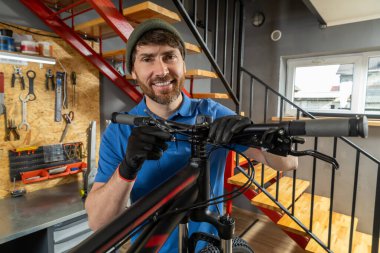 Sakallı tamirci arka planda penceresi olan bisiklet viteslerini tamir ediyor.