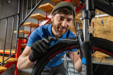 Deneyimli erkek bisikleti kırmızı merdivenli düzenli atölyede ustalıkla ayarlıyor.