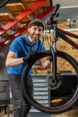 Deneyimli erkek bisikleti kırmızı merdivenli düzenli atölyede ustalıkla ayarlıyor.