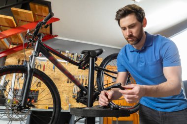 Deneyimli erkek bisikleti kırmızı merdivenli düzenli atölyede ustalıkla ayarlıyor.