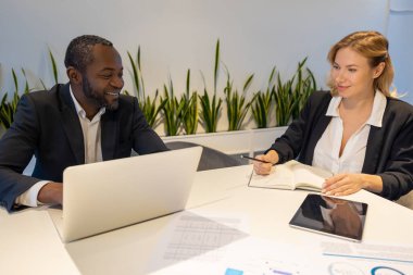 İş adamı ve iş kadını dizüstü bilgisayar ve tablet kullanarak birlikte çalışarak modern ofiste kapalı alandaki bitkilerle fikirleri tartışıyor.
