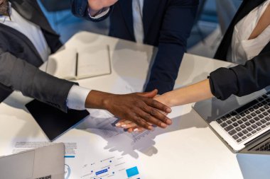 Modern ofiste masada oturan üç farklı iş arkadaşı takım başarısını kutlamak için el ele tutuşuyorlar.