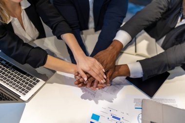 Toplantı masasında işbirliği yapan çok ırklı profesyoneller grubu proje üstüne olumlu bir jest yaparak el ele tutuşuyor.