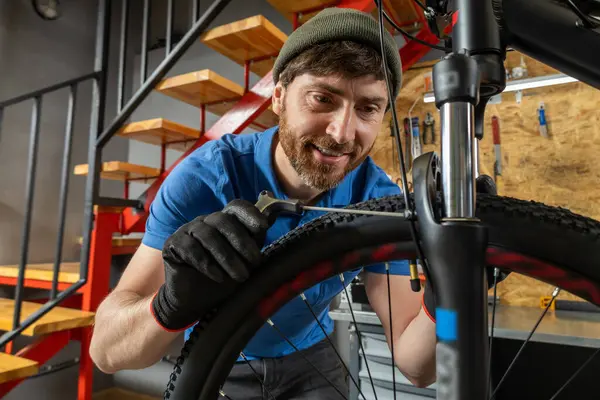 Deneyimli erkek bisikleti kırmızı merdivenli düzenli atölyede ustalıkla ayarlıyor.