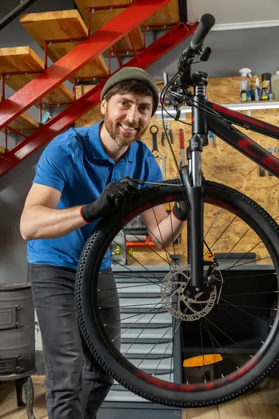 Deneyimli erkek bisikleti kırmızı merdivenli düzenli atölyede ustalıkla ayarlıyor.