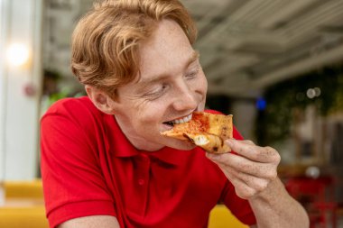 Pizzacıda. Genç kızıl adam pizza yiyor ve eğleniyor.