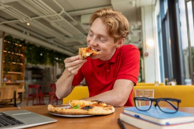 Pizzacıda. Genç kızıl adam pizza yiyor ve eğleniyor.