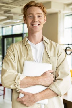 Bir kafede. Elinde dizüstü bilgisayarla bir kafede duran pozitif bir genç.