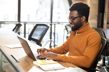 Ofiste. Ofiste çalışan, dizüstü bilgisayarı olan Afrikalı Amerikalı genç bir adam.