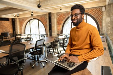 Ofiste. Ofiste çalışan, dizüstü bilgisayarı olan Afrikalı Amerikalı genç bir adam.