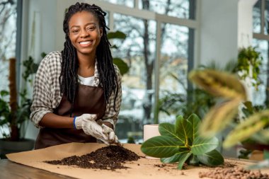 Çiçekçi. Memnun ve eğlenen genç bir kadın çiçek ekiyor ve meşgul görünüyor.