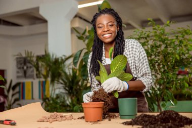 Bitki yetiştiriyorum. Gülümseyen çiçekçi asistanı çiçek dikiyor ve kendini iyi hissediyor.