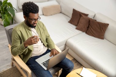 İnternette çalışıyorum. Kıvırcık saçlı, Afro-Amerikalı genç adam evden internet üzerinden çalışıyor.