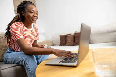 Görüntülü arama. Gülümseyen Afrikalı Amerikalı genç bir kadın dizüstü bilgisayarın başında oturuyor ve bir video görüşmesi yapıyor.