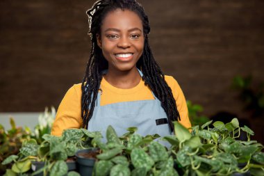 Çiçekli mutlu kadın. Gülümseyen Afro-Amerikan kadın çiçek saksılarıyla mutlu görünüyor.