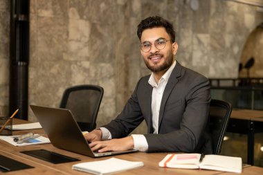 Ofiste. Koyu renk saçlı genç yönetici ofiste çalışıyor ve kendinden emin görünüyor.