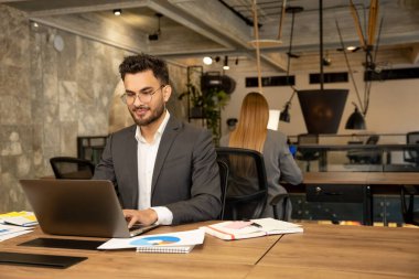 İşteki müdürüm. Beyaz bir erkek, ofiste çalışırken kendinden emin görünüyor.