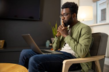 Düşüncelerle. Gözlüklü genç esmer adam çalışıyor ve düşünceli görünüyor.