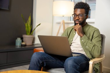 Düşüncelerle. Gözlüklü genç esmer adam çalışıyor ve düşünceli görünüyor.