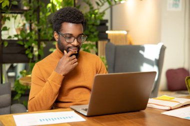 Odaklanmış Afrikalı Amerikalı adam uzak mesafe çalışması için dizüstü bilgisayar kullanıyor.