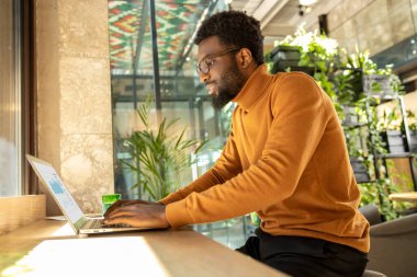 Erkek işyeri sahibi dijital araçlarla iş akışını yönetmek için masa başında oturmaktadır