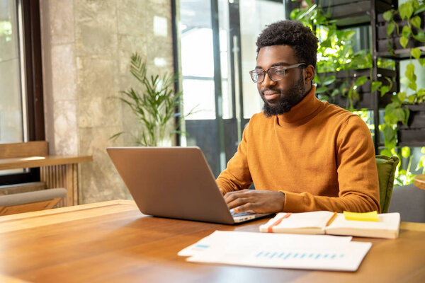 African American businessman in casual outfit managing business tasks on laptop in renovated loft office