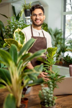 Çiçekçi. Çiçekçide gözlüklü genç adam mutlu ve gülümsüyor.