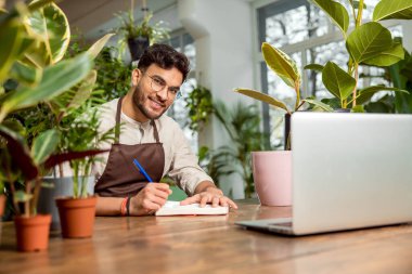 İş günü. Çiçekçide dizüstü bilgisayarda oturan genç adam.