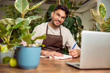İş günü. Çiçekçide dizüstü bilgisayarda oturan genç adam.