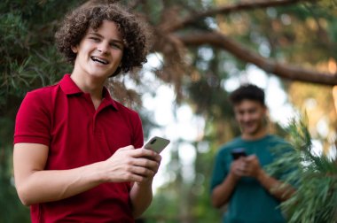 Parkta. Parkta ellerinde telefon olan iki genç.