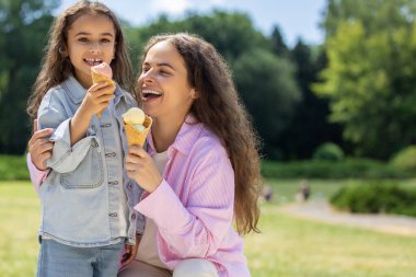 Genç anne ve kızı yaz parkında dondurma külahlarıyla gülüyorlar.