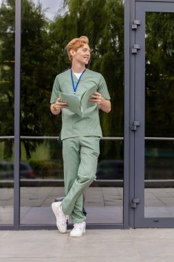 Cam klinik binasının yanında duran laboratuvar önlüklü kızıl doktorun elinde klinik geçmişi olan bir dosya var.