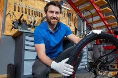 Profesyonel tamir atölyesinde lastik tamir eden kendine güvenen erkek teknisyen çekmeceler ve metal merdivenlerle çevrili.