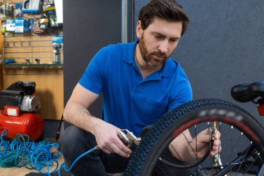 Modern atölyede bisiklet tekerini hava kompresörüyle şişiren odaklı bisiklet tamircisi