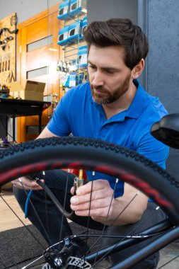 Mavi polo tişörtlü adam benzin istasyonunda bisiklet lastiğini şişirmek için kompresör kullanıyor.